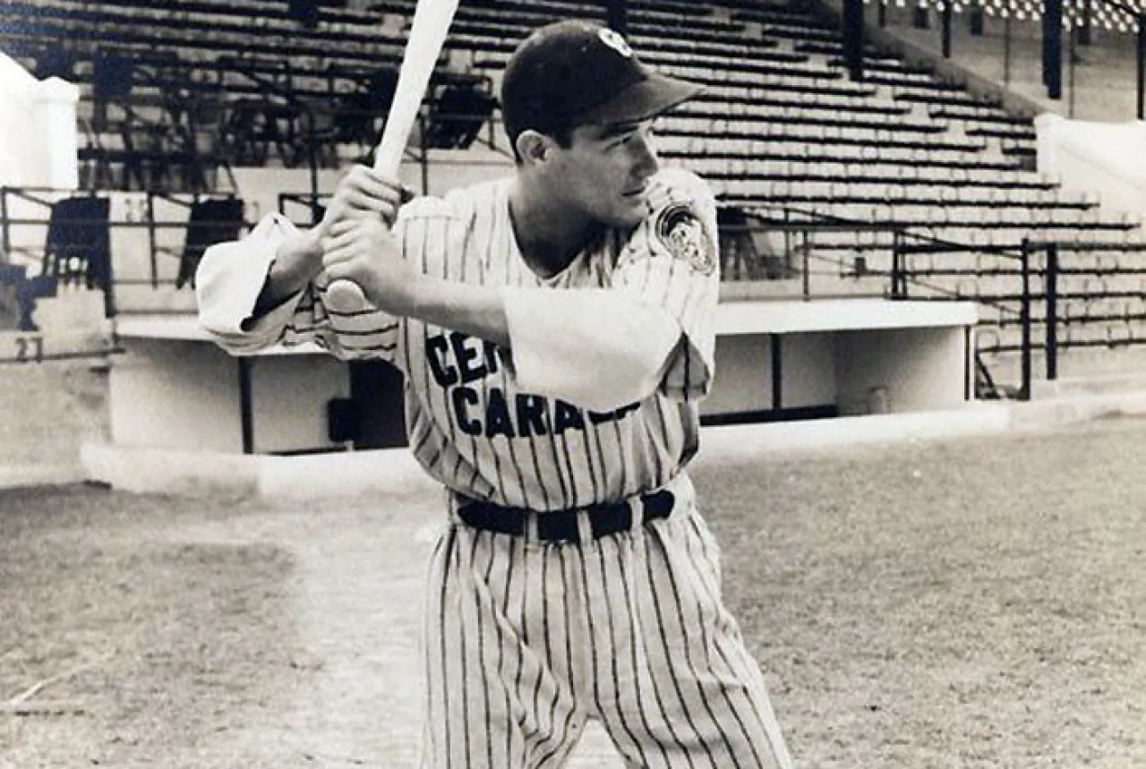 Alfonso “Chico” Carrasquel sostiene un bate y viste el uniforme de Cervecería Caracas en un estadio