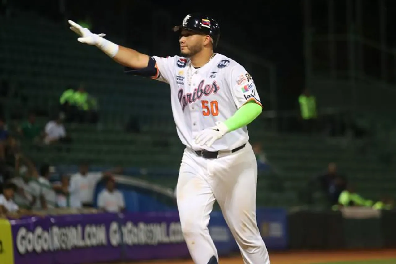 Omar Alfonzo, con uniforme blanco de Caribes y casco de bateo, extiende el brazo derecho sobre el terreno.