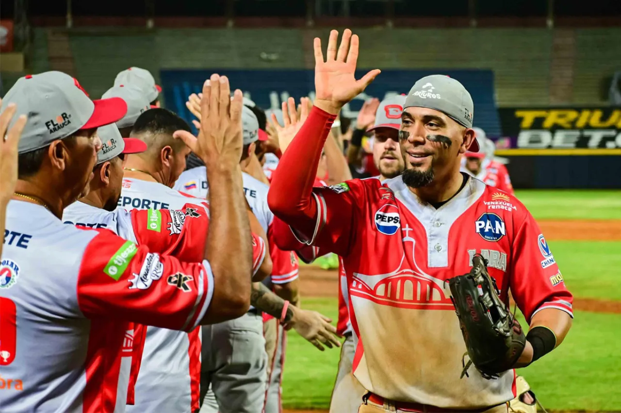 Rafael Ortega, con uniforme de Cardenales y guante en la mano izquierda, saluda a sus compañeros sobre el terreno.