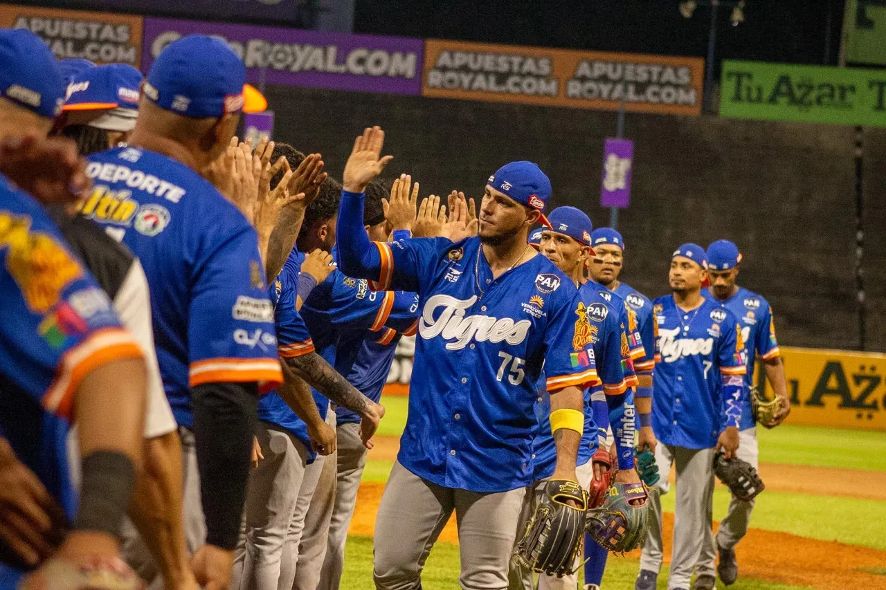 Peloteros de Tigres de Aragua, con uniformes azules y guantes, chocan las manos sobre el terreno del Estadio Universitario.