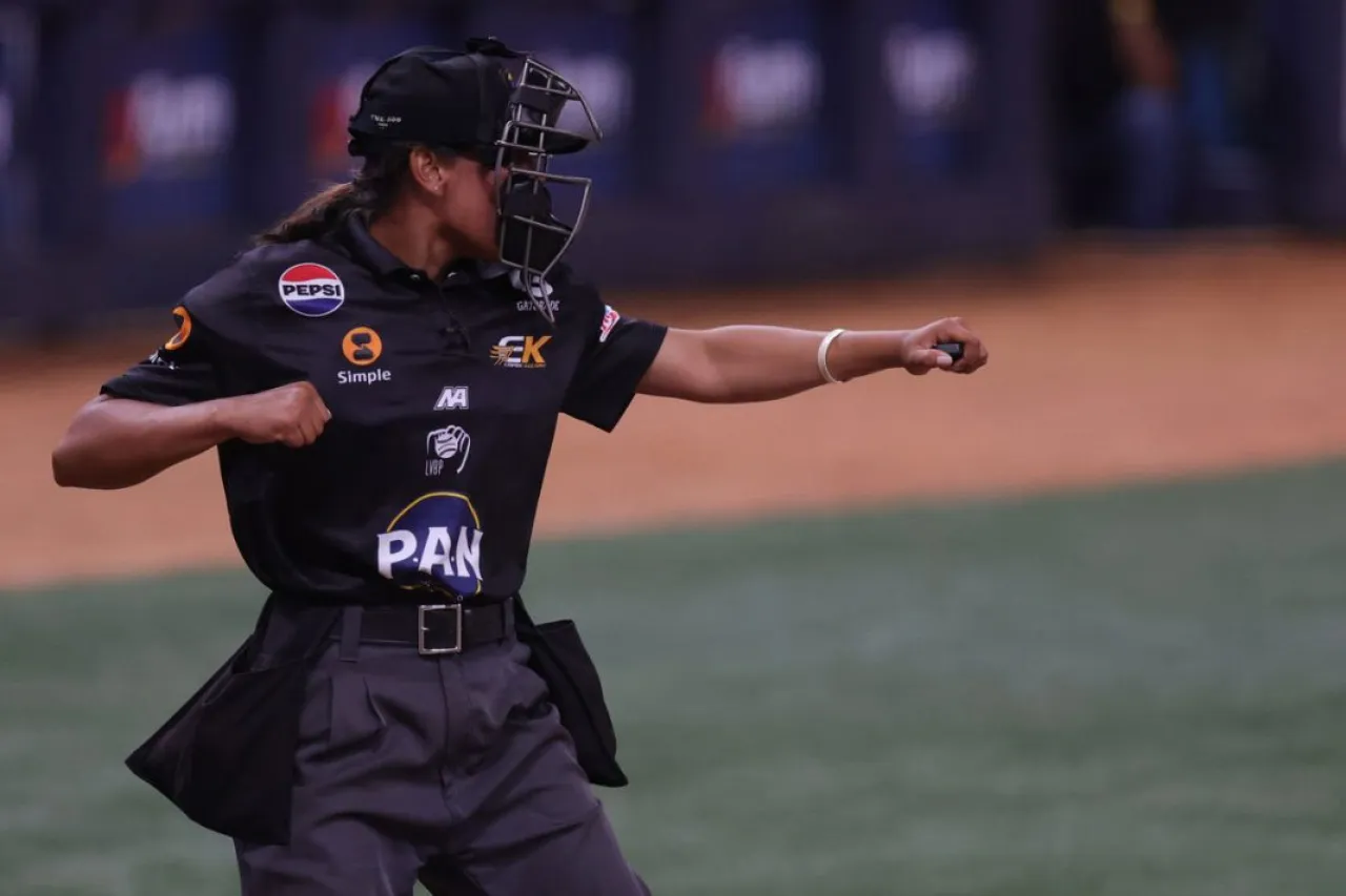 Wanda Rodríguez, con uniforme negro y careta, realiza una señal arbitral sobre el terreno.